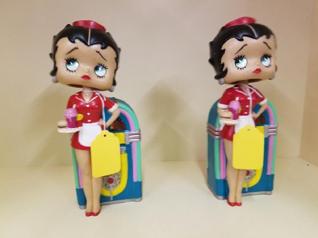 Two Betty Boop Bobble head Banks: Betty Boop in front of a jukebox. Two matching. 11.5 inches tall by 4 inches wide Betty Boop will serve up some fun! This 12-inch bobble bank features Betty Boop dressed in a cute waitress outfit, sta