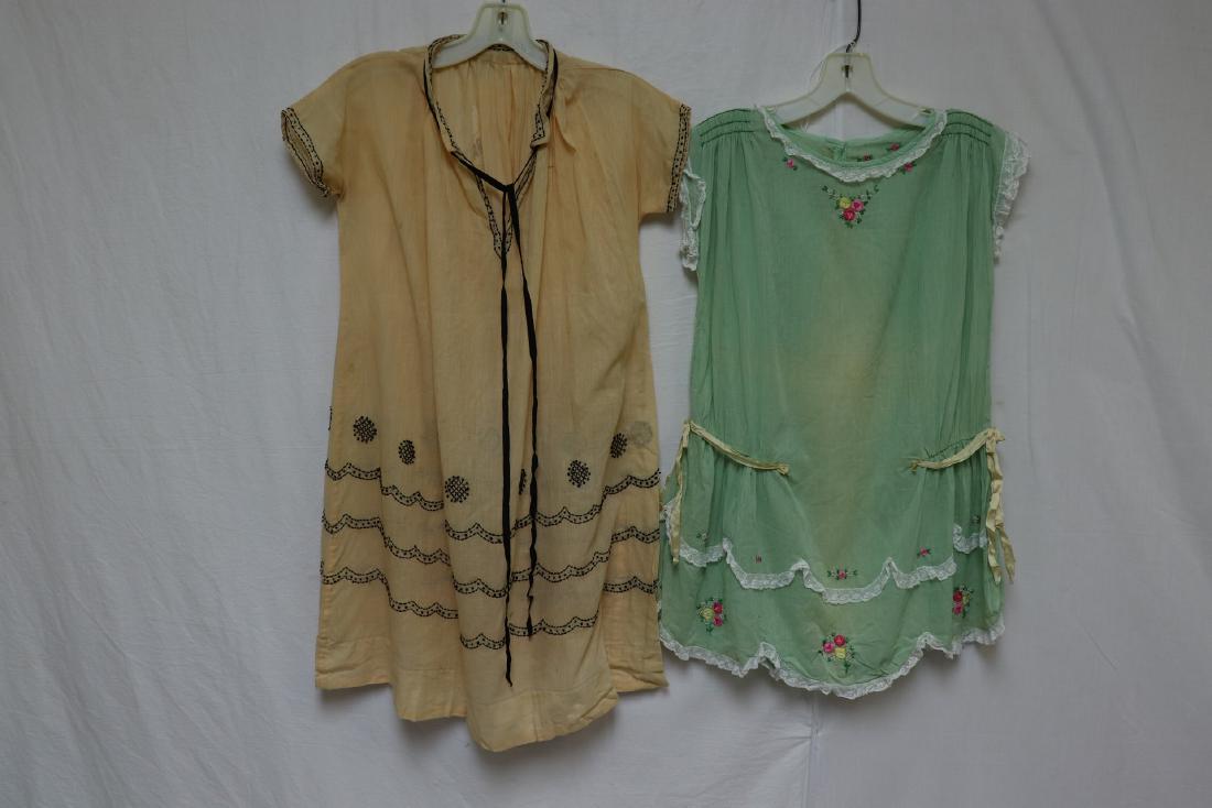 Lot Of 2 Early Girl's Dresses, Embroidery & Lace: Butter yellow w black embroidery, ribbon ties at neck. Good condition, 44" at bust with very light soil. Light green dress w ribbon detail and lace. Snaps at neck. 36" hip. Good condition with light f