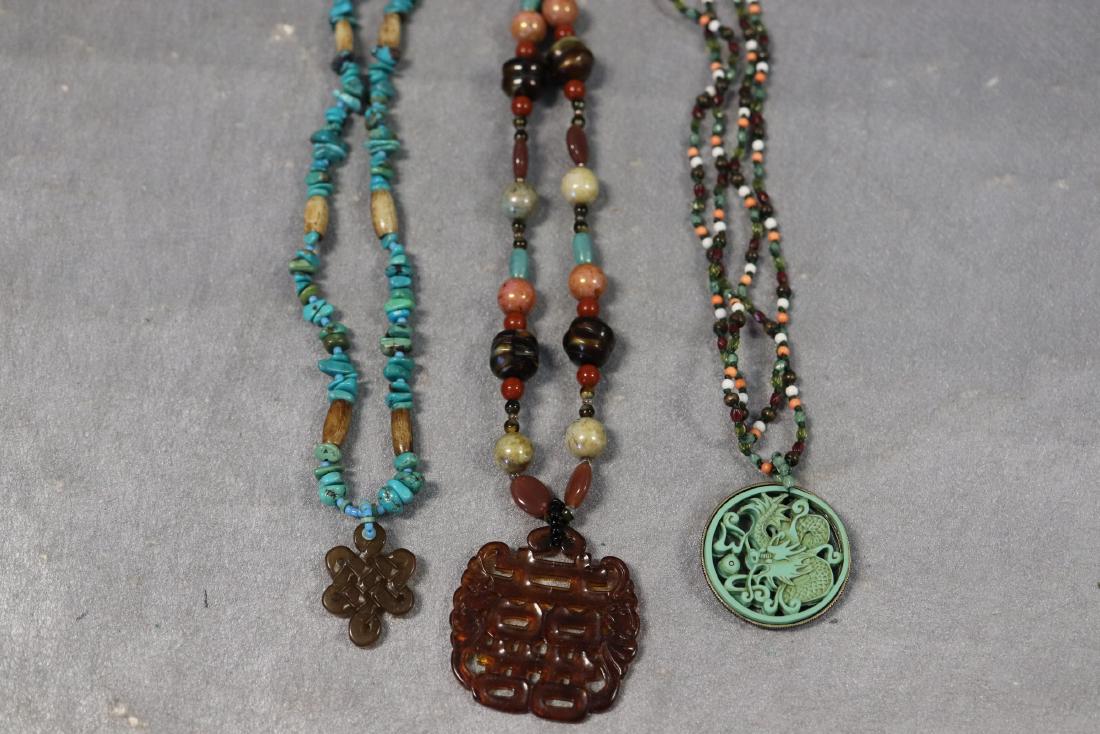 Lot of 3 Vintage Stone Necklaces With Pendants: Turquoise stones with bone bead spacers, amber colored stone medallion. Colorful stone necklace with Asian symbol medallion, marked KJL. Colorful seed bead necklace, hand knotted with green acrylic dr