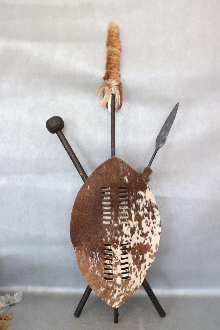 Nguni Hide Zulu Shield Tribal Art: Zulu shields are used for wedding and funeral ceremonies. Nguni hide, each pole is hand carved wood, one has metal spear. Measures approx. 47" long, 19" wide. Great condition.