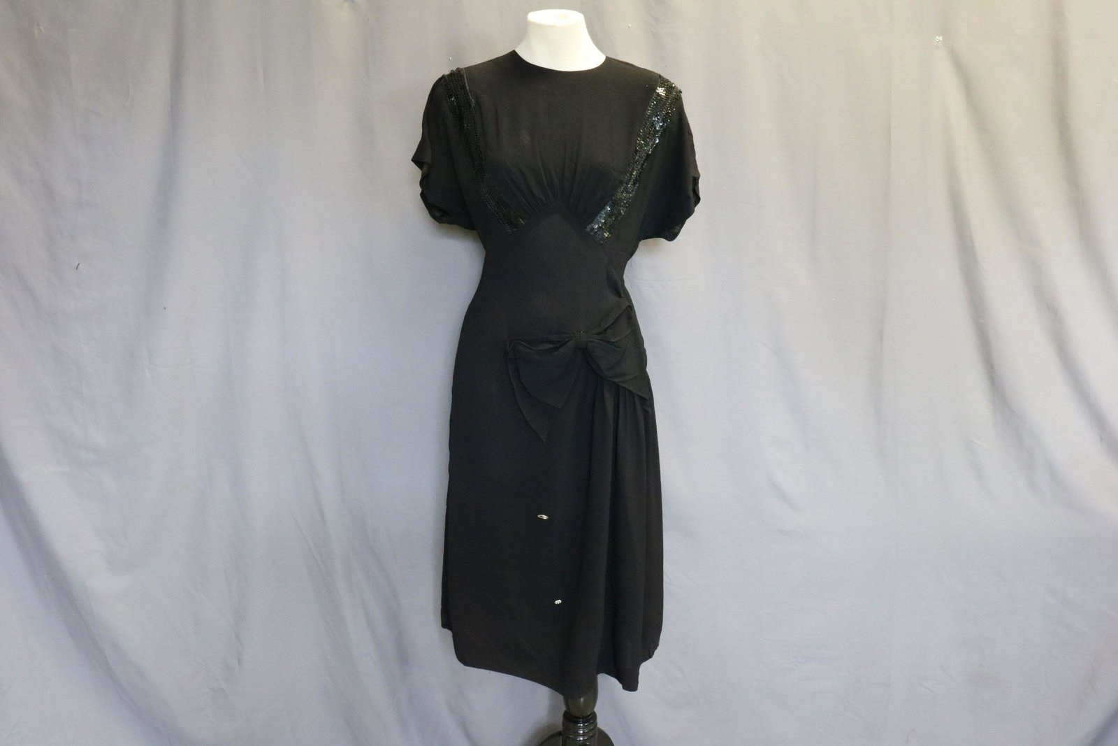 1940's Black Crepe Evening Dress with Sequins: Empire waist, sequins in front with gathers at bust, attached bow at hip, side buttons, buttons in upper back (they are unmatched and 2 are missing). Some small seam repair needed at side seam.