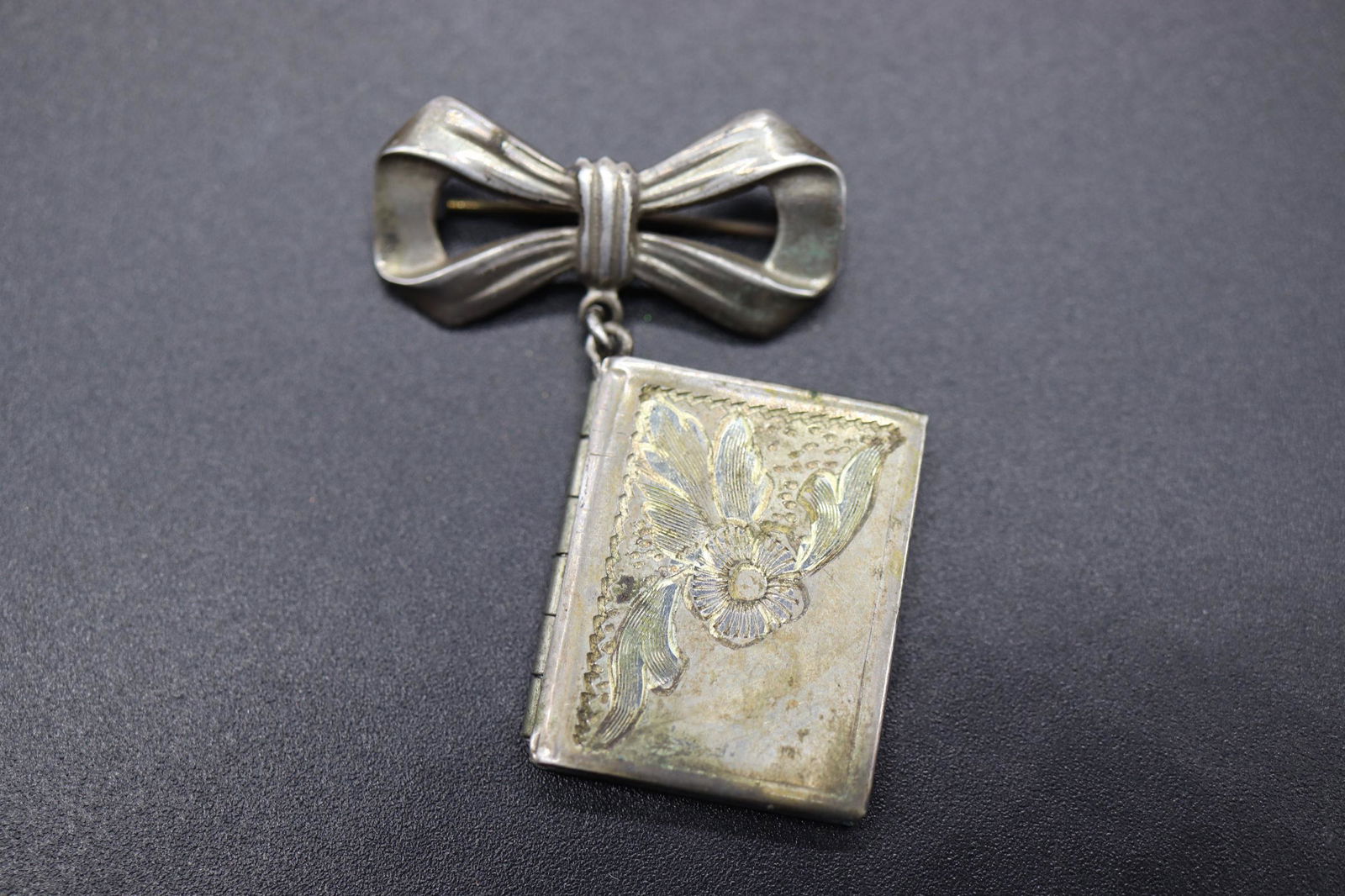 Antique Sterling Silver Book Locket Brooch: bow pin with hanging etched book locket, tiny pictures inside, marked sterling