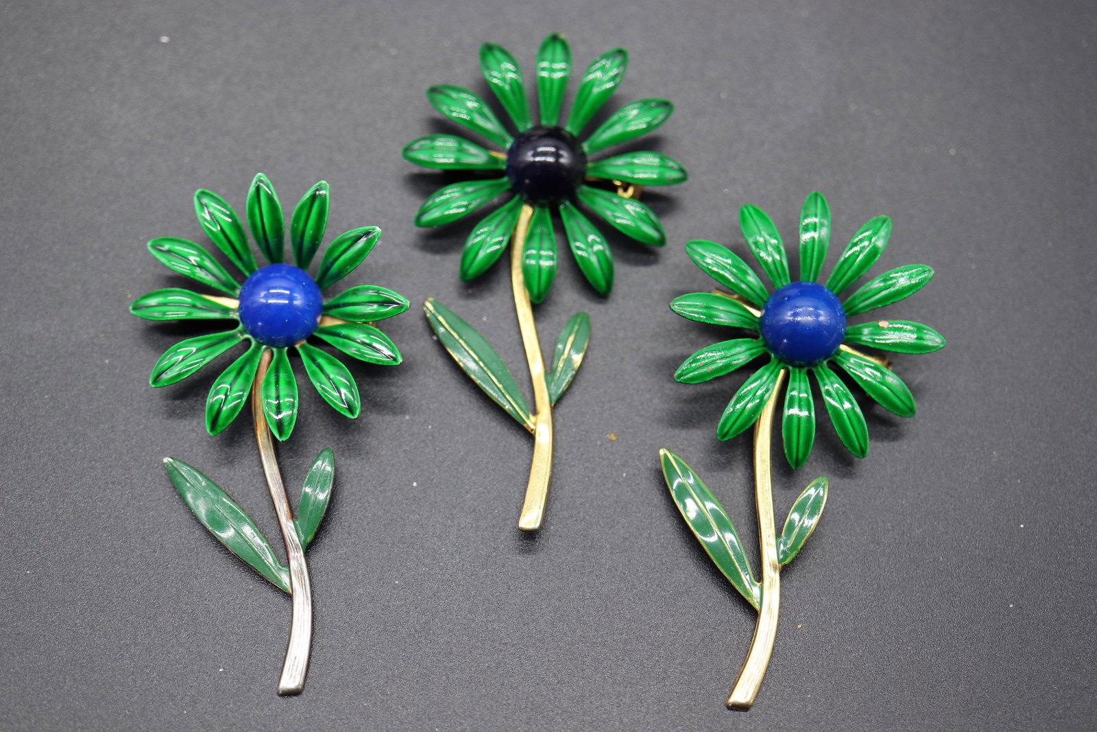 Lot of 3 Vintage Enamel Flower Brooches: silver Tone with green petals and blue center, two gold tone one with blue center the other with black center, approx. 2 3/4 inches tall each