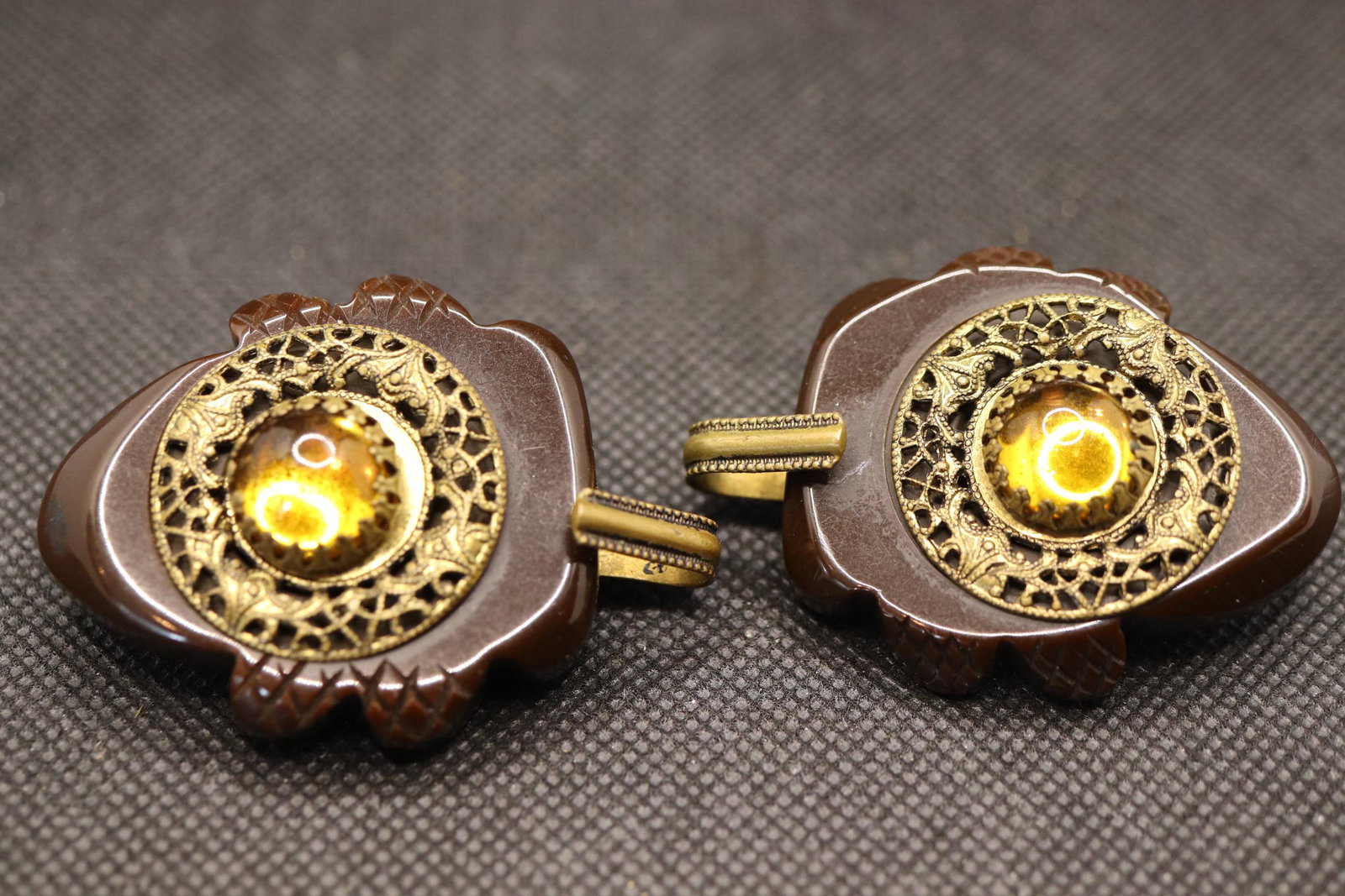 Pair of Vintage Bakelite Hook Style Buttons with Gold: brown carved bakelite with gold tone metal inlay and round gold stone center with hook for closure. Approx. 2 1/4 inches overall