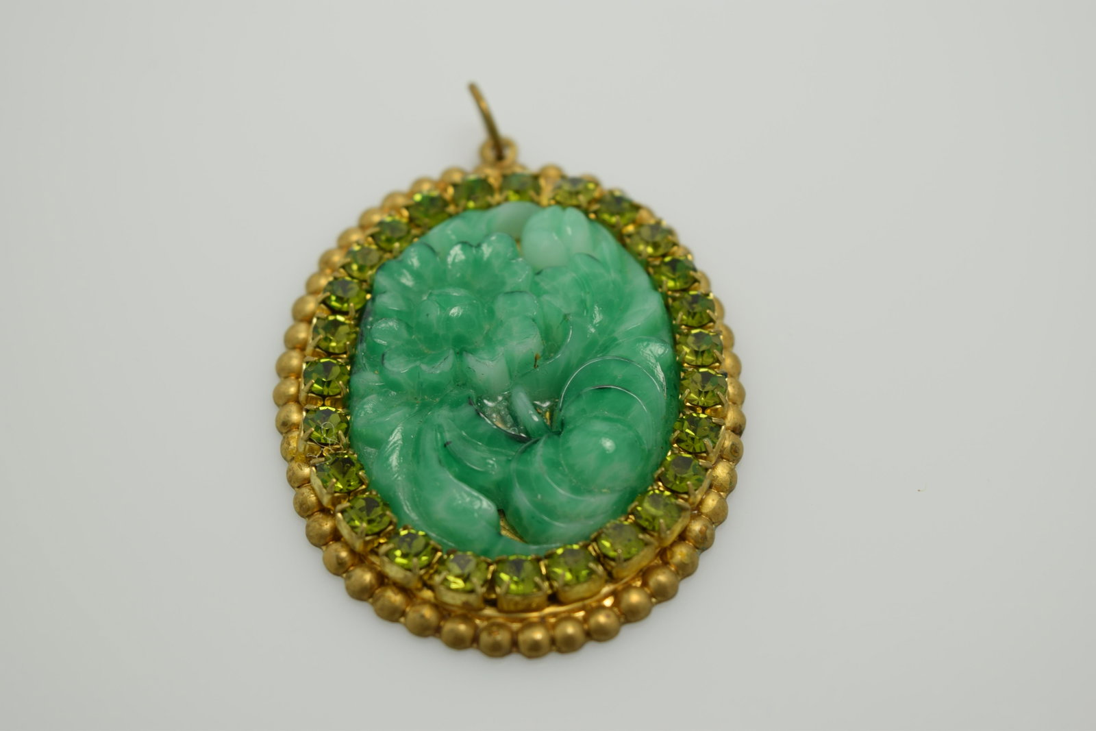 Vintage Carved Jade Oval Floral Pendant with Green: approx. 2 1/4 inch oval pendant in gold tone setting, hand carved jade center with faceted lighter green stones around edge