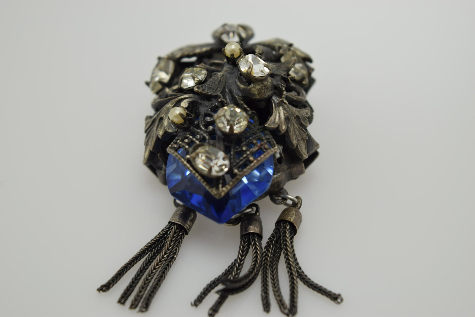 A vintage dark silver tone pin/brooch/pendant with: An approx. 2" long (including 3 set of tassels) dark silver tone pin/pendant. It is set with clear prong set rhinestones & 1 odd shape cobalt stone. It is in pre-owned condition.