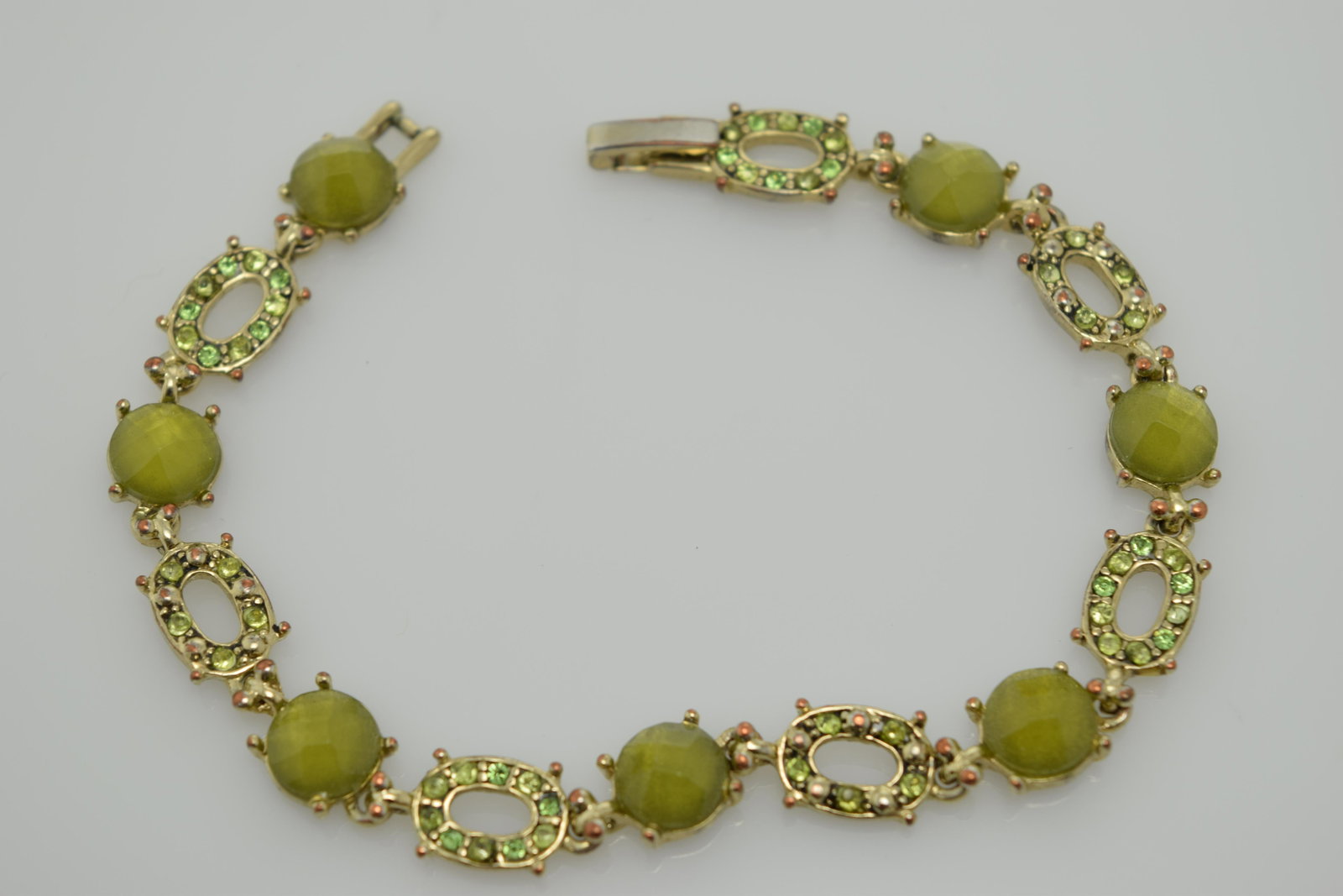 A silver tone bracelet in shades of green.: a 7-1/4" silver tone bracelet with shades of green rhinestones and faceted plastic stones. There is wear on the metal on the back of the bracelet. Front is fine.