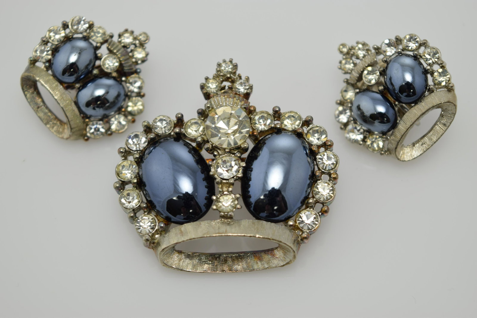 A vintage set of crown shaped pin/brooch and earrings.: A vintage pin & clip on earring set shaped like crowns. It is set in silver tone metal with wear to the back of the pin. The pin can also be worn as a pendant. The crowns are made of 2 grey oval faux 