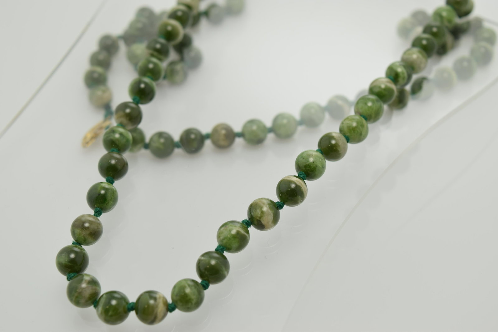 A long necklace of shades of green stone ball beads.: A long (approx. 32") necklace of 8mm ball beads made of shades of green stone. The beads are hand tied. In good condition.