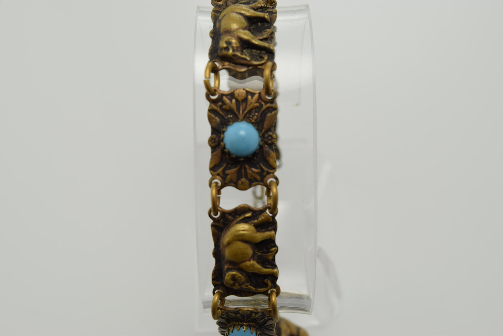 A brass color bracelet with elephants and turquoise: A brass color adjustable 6-1/4"-8" bracelet made up of 7 panels-4 with turquoise glass cabochons & 3 with elephants. There is an adjustable chain that has an elephant charm hanging from it. It is in g