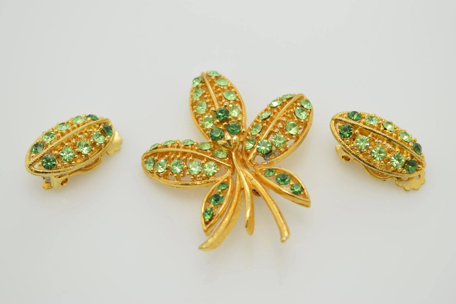 A vintage pin and earring set with shades of green: A vintage gold tone pin & clip on earring set with shades of green rhinestones. In good condition.