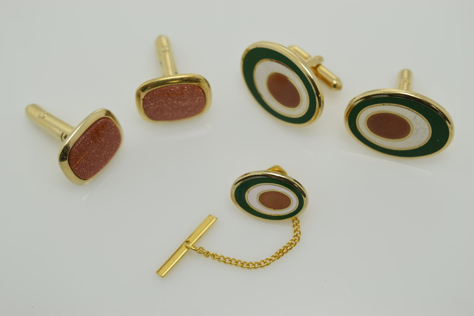 A lot of a pair of cuff links and a tie tack and cuff: This lot has a pair of gold stone cuff links and a set of green, brown, & white enamel cufflinks and tie tack set. All are set in gold tone meta; and are in good condition.