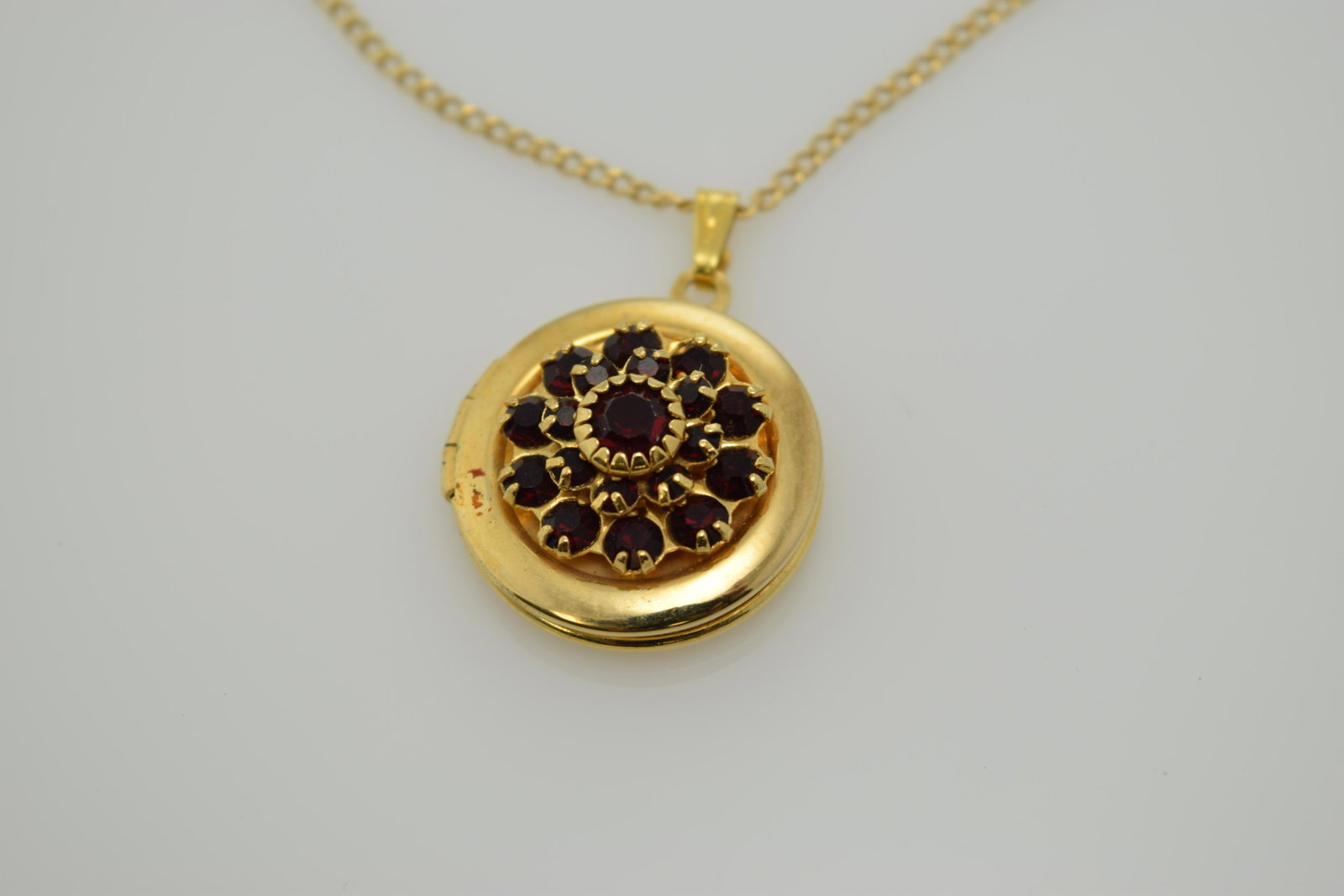 New gold tone locket with red rhinestones.: A gold tone, round locket with red rhinestones on an 18" chain. Locket is approx. 3/4" not including bale. In good condition.