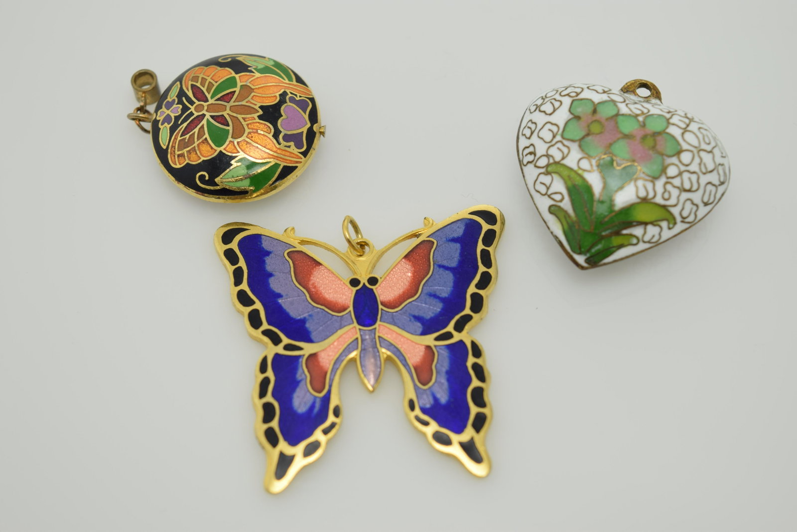 A lot of two vintage pendants and an enamel butterfly: This lot contains 2 vintage cloisonne pendants-1 being heart shaped with white & green cloisonne. The other is round & has a black cloisonne back ground with a colorful stylized butterfly. The modern 