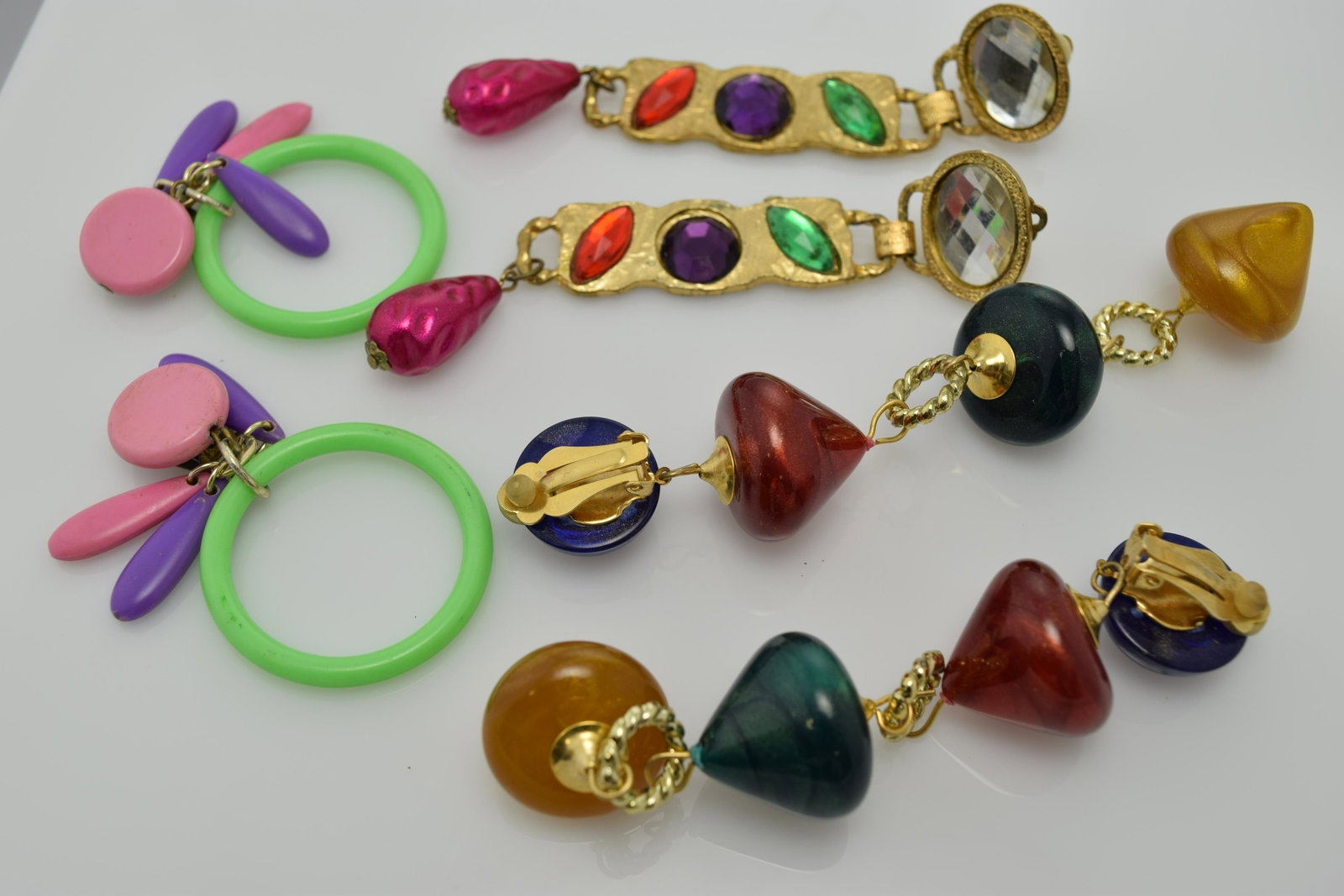 A lot of three pairs of funky clip on earrings.: A lot of 3 funky clip on earrings. A pair of pink/purple/ and green plastic earrings. A pair of very long (4-3/4") with 4 cone shaped plastic beads (dark green, golden, dark red). And a 4" long pair o