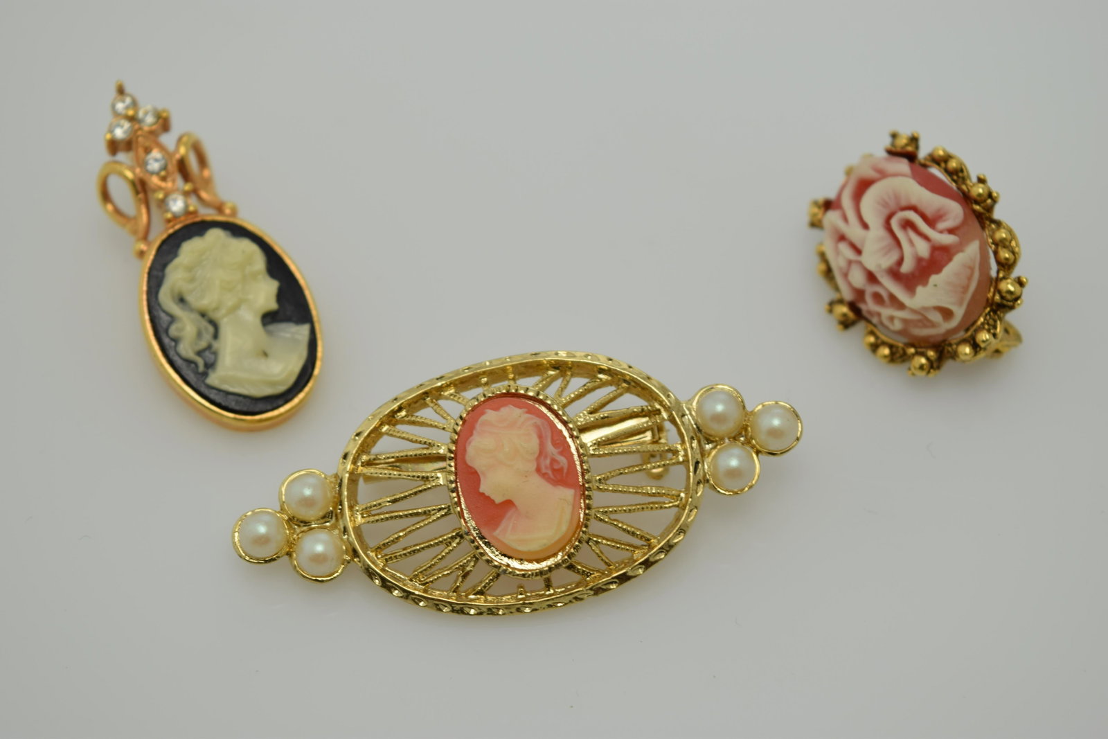 A lot of three faux cameo pins.: A lot of 3 gold tone faux cameo pins. The black & white cameo pendant marked GECFJ. The other 2 are coral colored. All are in good condition.