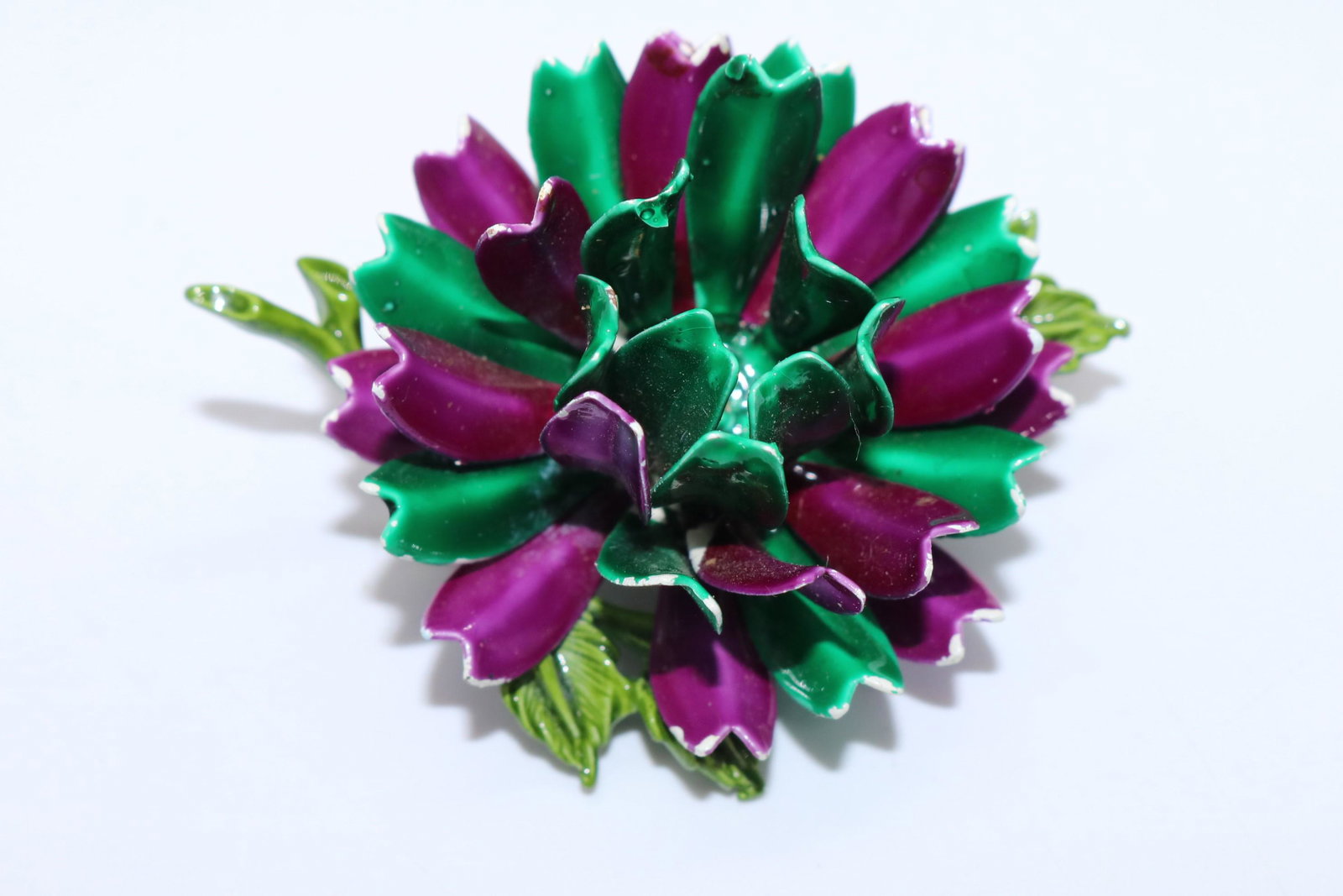 A 1960's enamel green and purple flower pin.: An approx. 1-1/2" x 1-1/2" 1960's enamel flower pin. It has green & purple petals w white tips. It is in pre-owned condition.