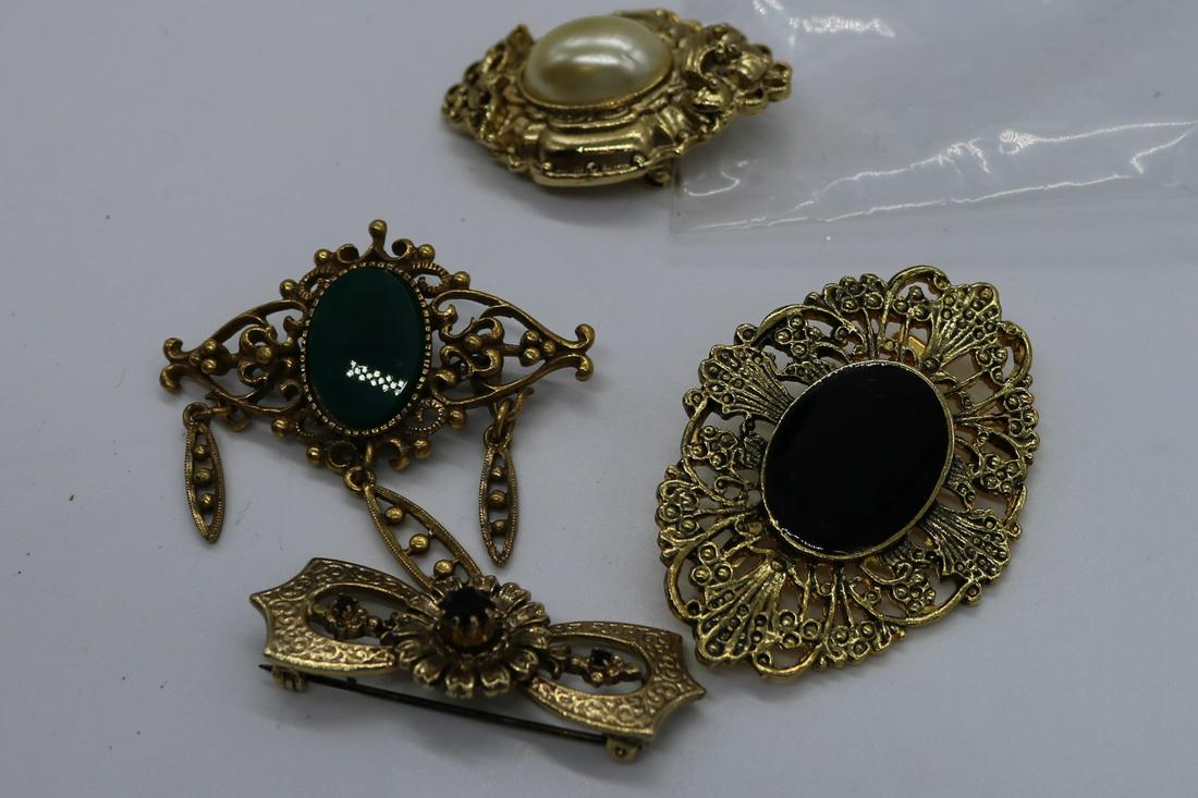 A lot of four vintage, gold tone pins/brooches.: A lot of 4 gold tone pins. 1st has a green oval stone & 3 dangles, the 2nd has a black oval plastic stone center, the 3rd has an oval faux pearl center, & the 4th is a bow pin dark red rhinestones. Th