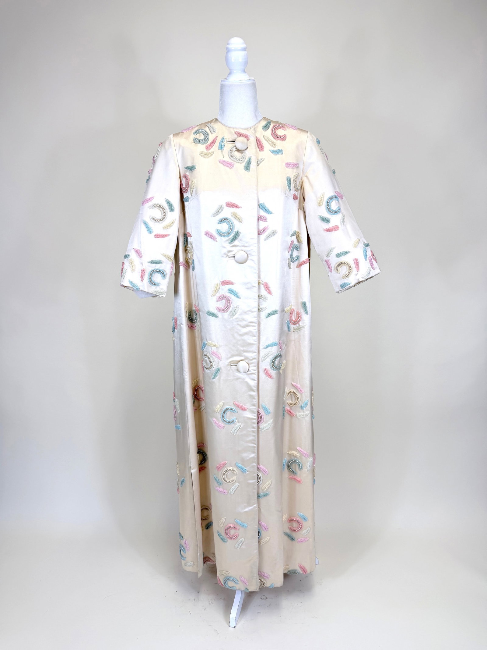 3-D BEADED IVORY SILK SATIN EVENING COAT, 1960s: SH-SH 18", L 54", interior hem stained, few holes/pulls to embroidery, 1 button detached, see photos. Provenance: From the M. Estella Sprague Costume Collection