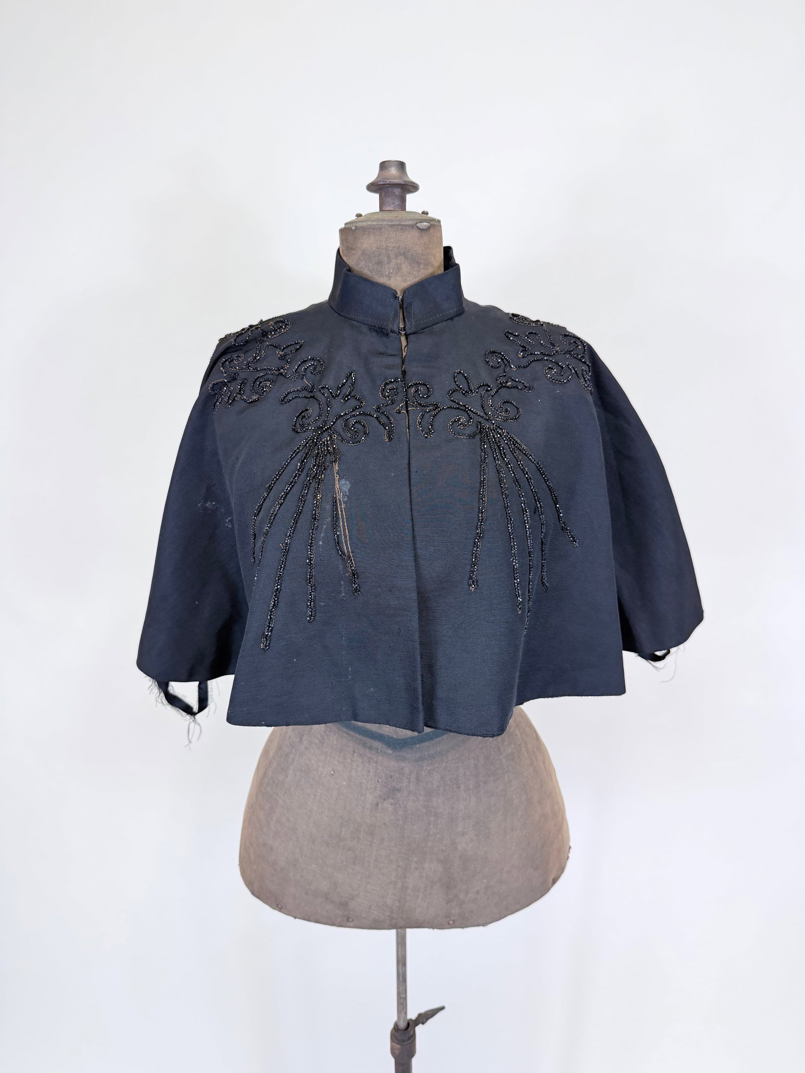 JET BEADED SILK FAILLE CAPELET, 1880s-1890s: L 18", some residue spots, damage to hem facing, some wear around collar, some bead loss, see photos.