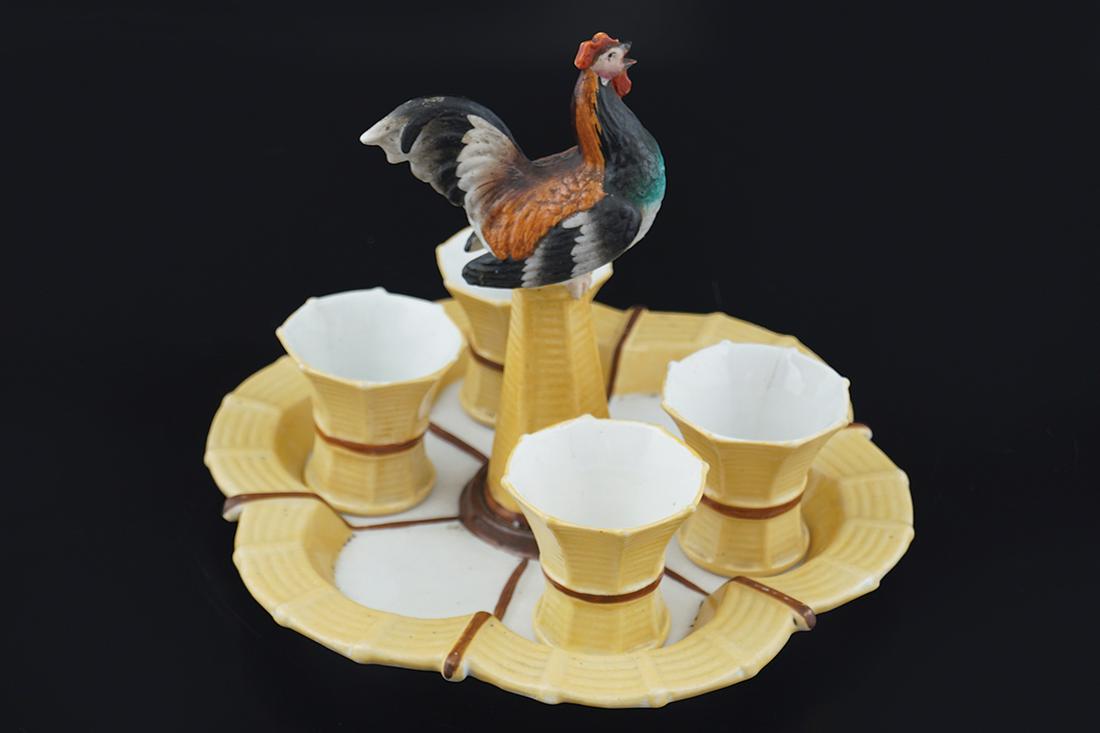 19TH-CENTURY PORCELAIN EGG EPERGNE: of four egg cups in a circular serpentine tray, surmounted by a bird 18 cm. high; 20 cm. diameter