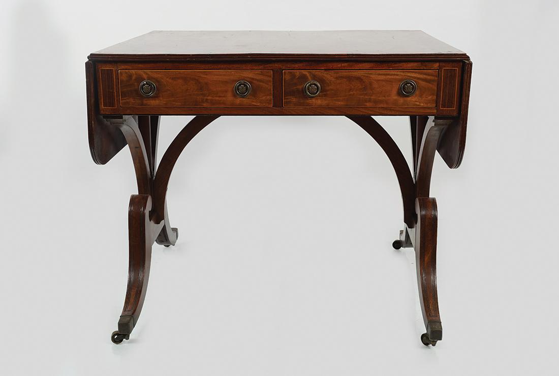 REGENCY PERIOD MAHOGANY SOFA TABLE: the ebony string inlaid rectangular shaped top with D-shaped drop leaves, above two real and opposing faux drawers, raised on sabre ends, terminating on brass feet and casters 80 cm. high; 80 cm. wide