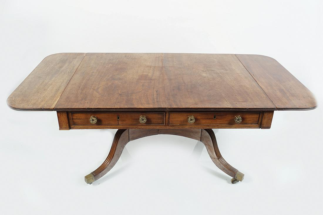 REGENCY MAHOGANY COFFEE TABLE: the rectangular reeded edged top, with D-shaped drop ends, raised on turned pillars, supported on a sabre legged pod, terminating on brass feet and casters 74 cm. high; 100 cm. wide; 79 cm. deep