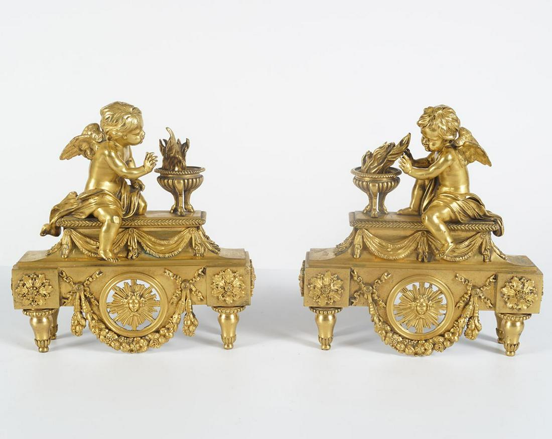 PAIR OF REGENCY ORMOLU FIRE DOGS: each depicting a cherub warming his hands, mounted on a canapÃ©. Each 29 cm. high; 26 cm. wide