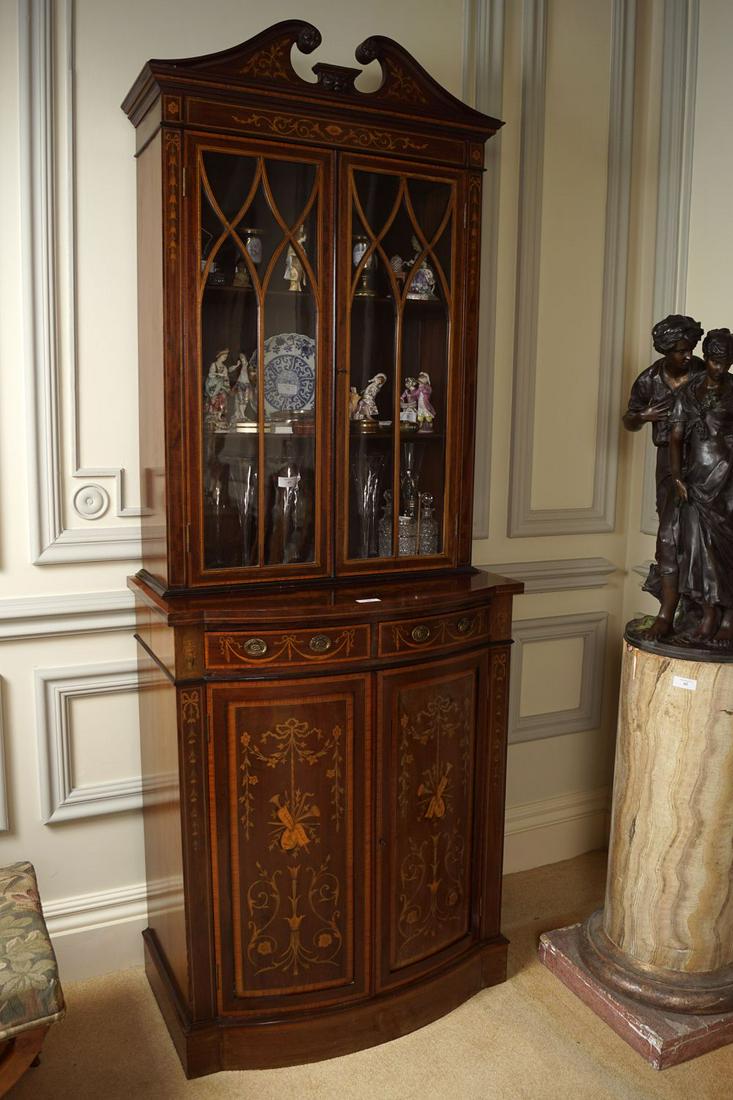 EDWARDIAN MAHOGANY AND MARQUETRY CABINET: by S & J Jewel, London. The superstructure with 2 glazed doors enclosing shelves, below a broken arched swan necked pediment. The projecting bow front base, with 2 frieze drawers over 2 profusely inla