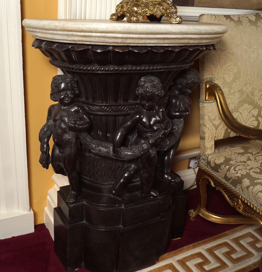 PAIR OF ROCOCO BRONZE CONSOLE TABLES: each with a statuary white marble demi-lune shaped top above a volute capital fronted by cherubs holding bell petal swags, raised on a carved and stepped breakfront plinth. 99 cm. high; 77 cm. wide; 3