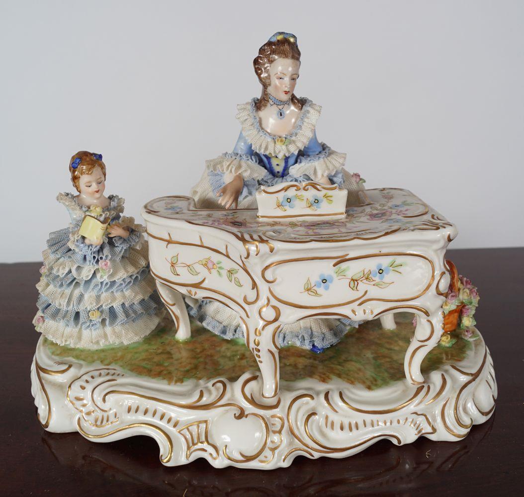 GERMAN PORCELAIN GROUP: Woman playing piano, and a child reclining, raised on an oval serpentine, rococo scroll decorated base 18 cm. high; 24 cm. wide