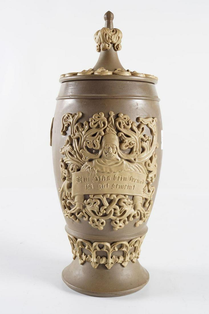 ARMORIAL SALT GLAZED BEER STEIN: with raised decoration depicting Gambrinus. Inscribed "Ein glas beim freund ist gut gemeint", with Gothic tracery panelled lid. 30 cm. high