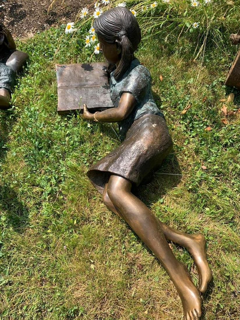 BRONZE GARDEN SCULPTURE: Figure of a young girl reclining reading a book. 40 cm. high; 120 cm. wide Approximate Time: 10:25 Lot No: 29 Category: Garden & Decorative Objects