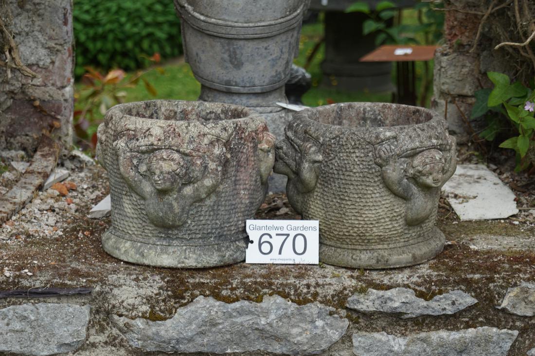 PAIR OF MOULDED STONE GARDEN URNS: each of vase shape with raised moulded cherub decoration, raised on a circular foot. 21 cm. high; 24 cm. in diameter; Approximate Time: 15:02 Lot No: 670 Category: Garden & Decorative Objects