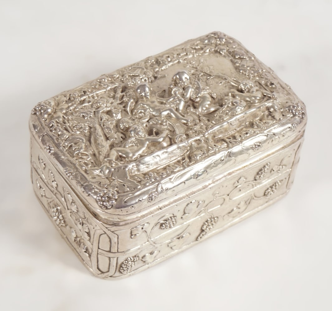 SILVER BOX: the lid with bacchanalian figures enclosed by vine leaves, the body decorated with grapes and leaves. London 1897. Makers: Edwin Thomson Bryant. 7 cm. high; 14 cm. wide; 9 cm. deep; 468 grams; Approxi
