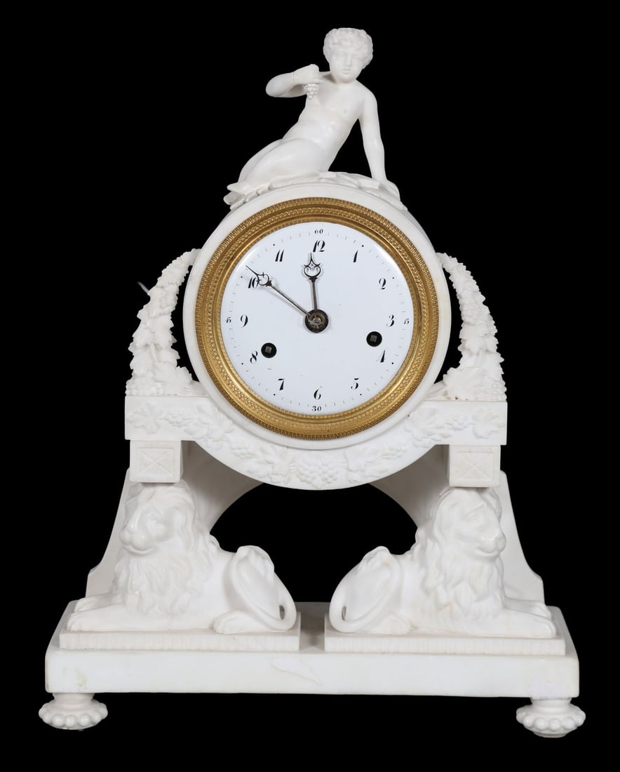FRENCH EMPIRE PERIOD CARVED MANTEL CLOCK: The circular enamel dial within a white marble case surmounted by a classical figure and flanked by recumbent lions, with gilt-metal mounts. CLOCKS AND BAROMETERS