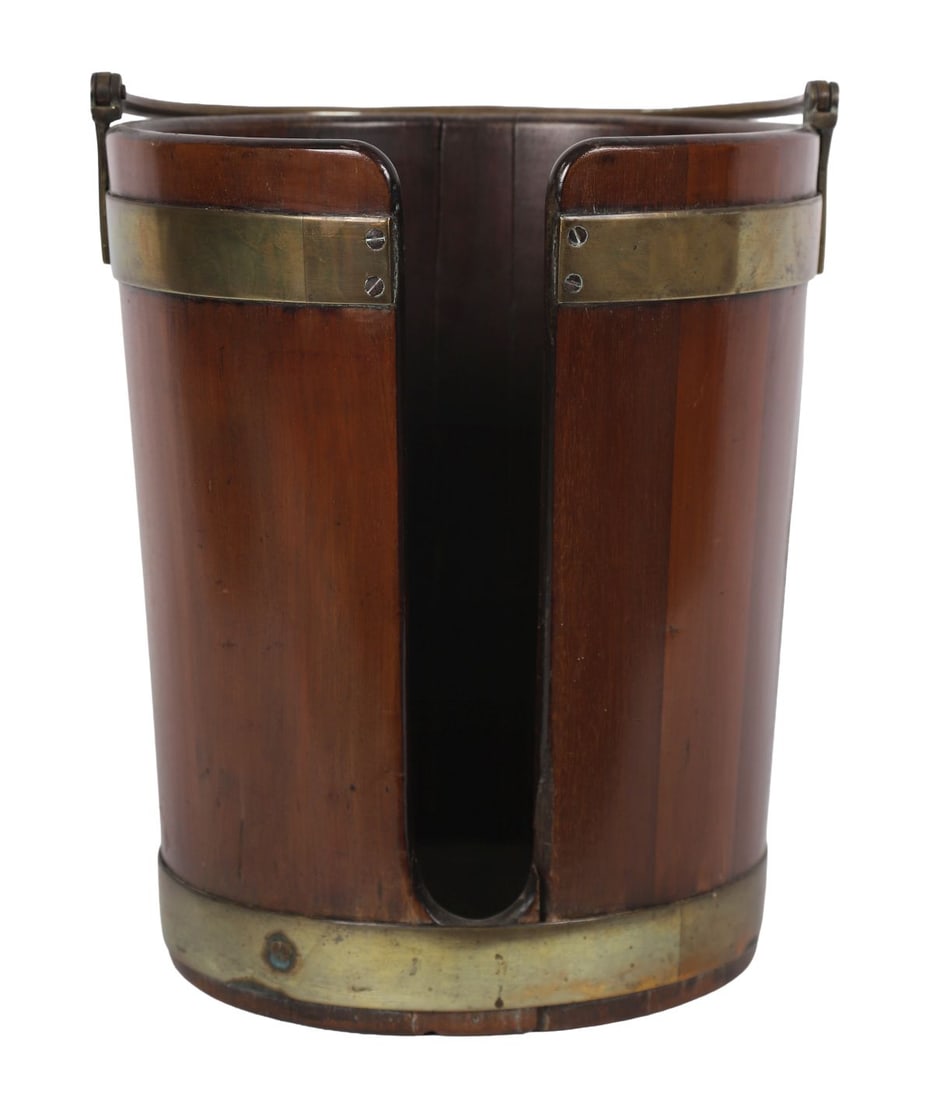 GEORGE III MAHOGANY AND BRASS-BOUND PLATE BUCKET: An oval mahogany plate bucket with brass bands and swing handle, designed to hold dinner plates. FURNITURE