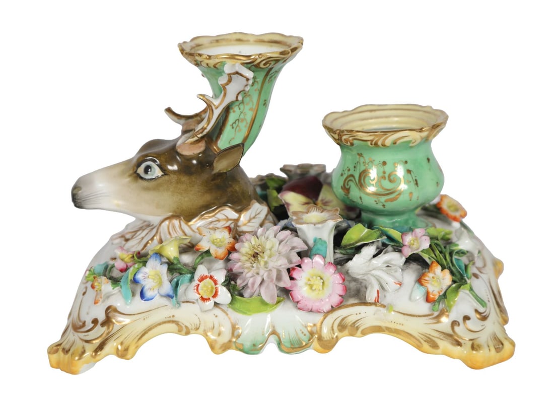 19TH-CENTURY CONTINENTAL PORCELAIN INKSTAND: Modelled with twin inkwells and pen rests, surmounted by a stag’s head and decorated with applied flowers and scrolling gilt detail. PORCELAIN