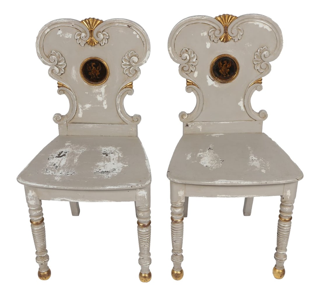 PAIR OF REGENCY PAINTED ARMORIAL HALL CHAIRS: PARCEL GILT, A pair of Regency hall chairs, painted and parcel gilt, each with shaped backs centred by armorial roundels, raised on turned front legs. FURNITURE