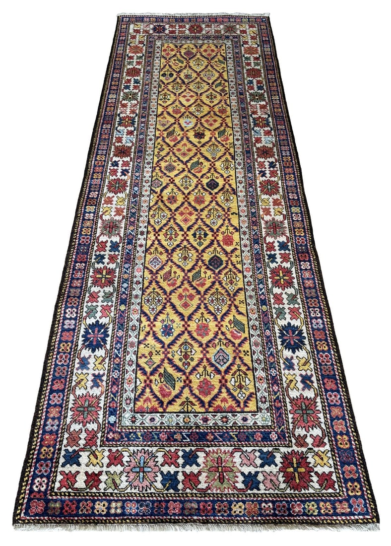 20TH - CENTURY DAGESTAN (N.E. CAUCASUS) LONG RUG: The golden field with an all-over lattice of geometric lozenges and stylised floral motifs, enclosed within multiple borders of bold Caucasian geometric design. CARPETS AND RUGS