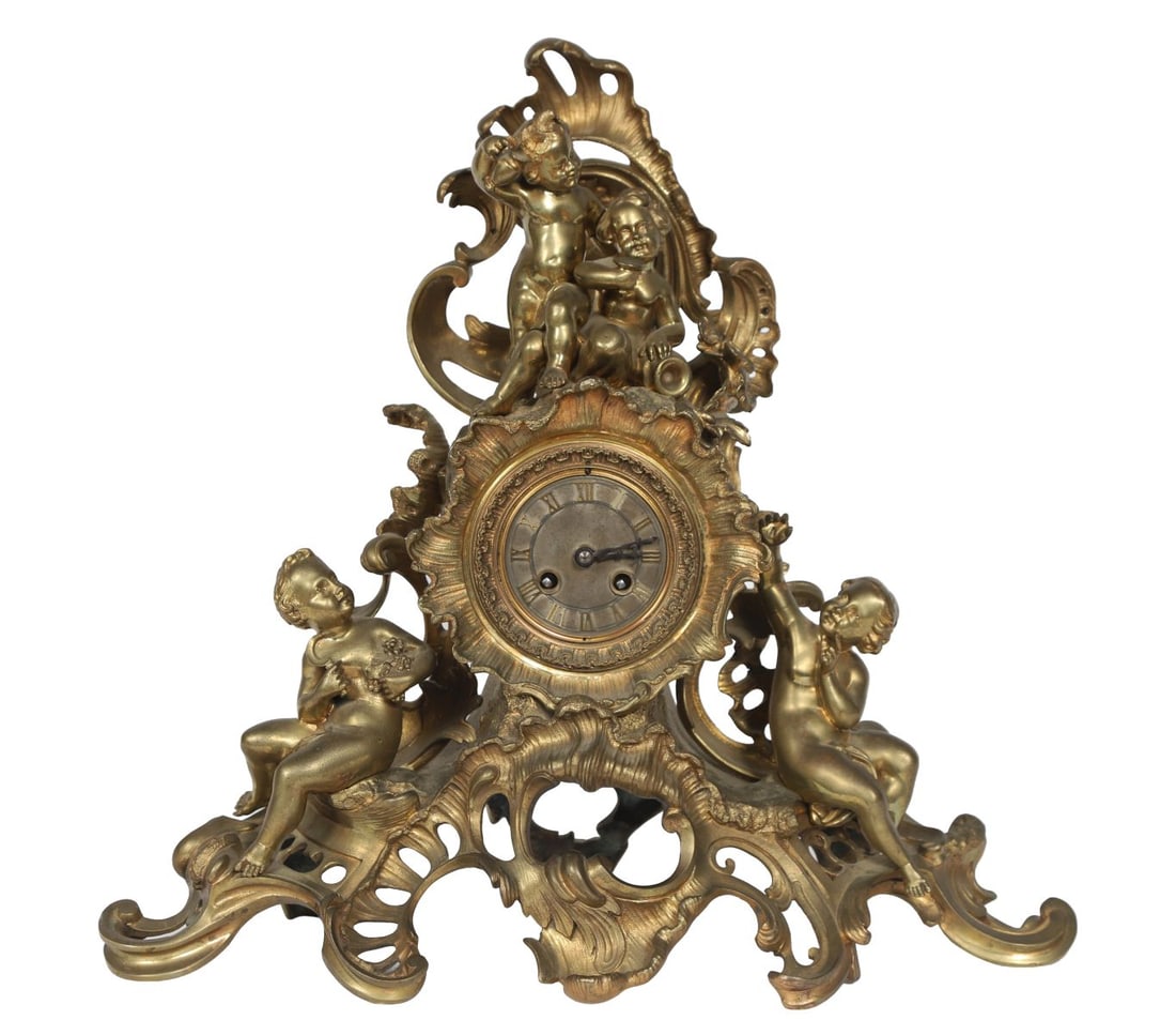 19TH-CENTURY FRENCH ORMOLU FIGURAL MANTEL CLOCK: The case surmounted by putti within scrolling rocaille ornament, the circular enamel dial with Roman numerals, the base with further applied cherub decoration. CLOCKS AND BAROMETERS