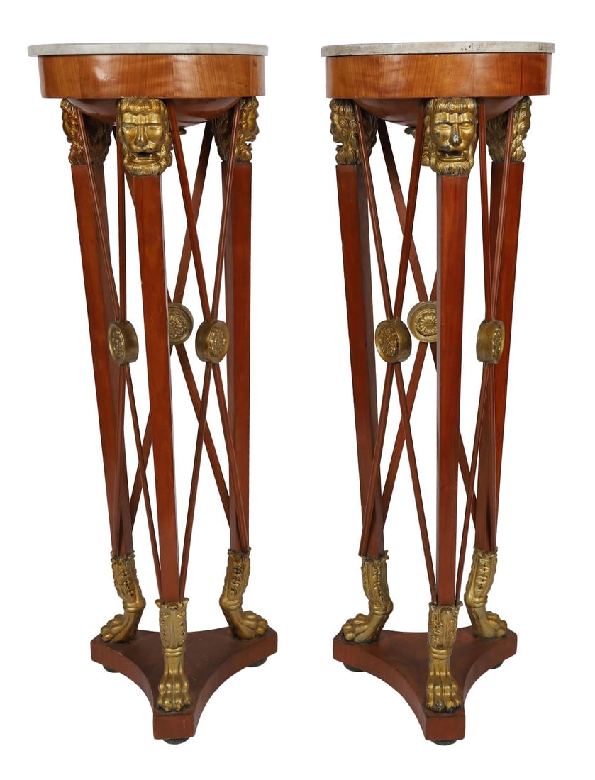 PAIR OF FRENCH EMPIRE STYLE MAHOGANY TORCHÈRES: PARCEL GILT, A pair of torchères, each with circular marble top above tapering supports mounted with carved lion masks and gilt paw feet, united by stretchers. FURNITURE
