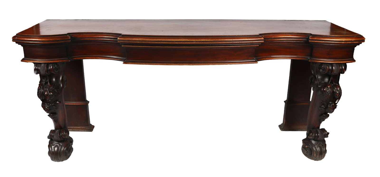 IRISH REGENCY INVERTED BREAKFRONT SIDE TABLE: BY MACK, WILLIAMS AND GIBTON A large Regency Irish mahogany side table of serpentine outline, the moulded top above a shaped frieze, raised on boldly carved scroll supports with deeply undercut acanth