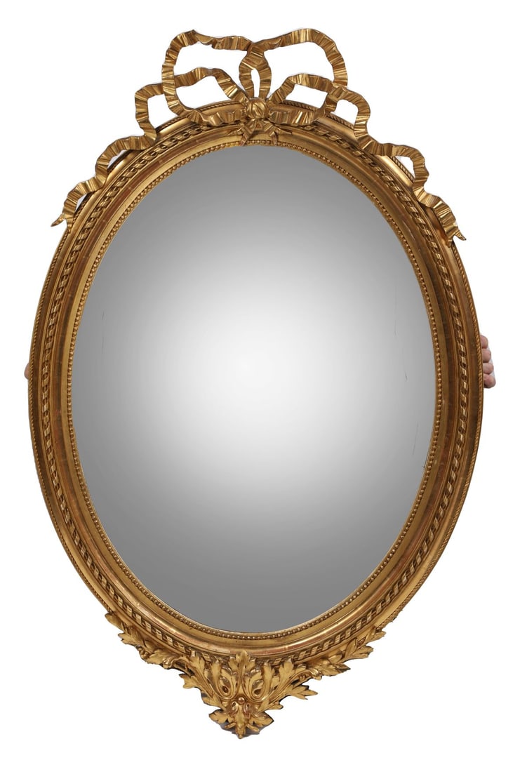 19TH-CENTURY GILT-FRAMED OVERMANTEL MIRROR: A 19th-century giltwood overmantel mirror of oval form, the frame richly carved with scrolling foliage, ribbon and floral motifs. Retaining the original mirror plate within a shaped surround. Continen