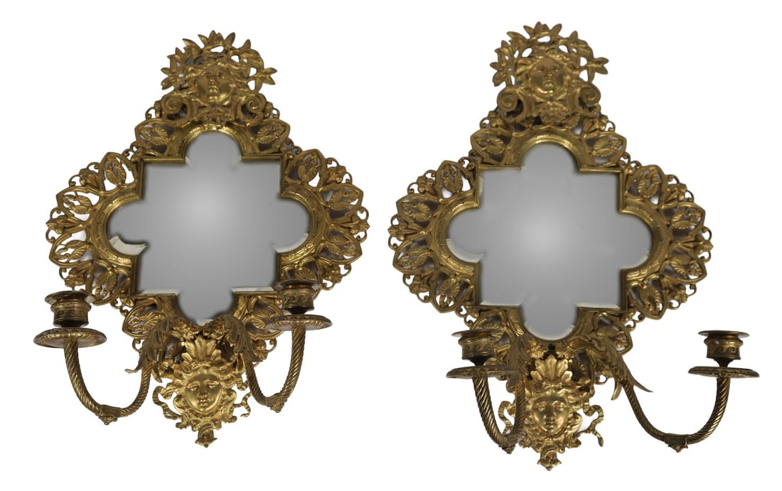 PAIR OF 19TH-CENTURY MIRROR-BACK WALL SCONCES: ORMOLU-MOUNTED, Each of scrolling Rococo form, the shaped mirror plates within richly cast ormolu frames incorporating foliate and mask ornament, issuing single acanthus-cast branches with drip pans a