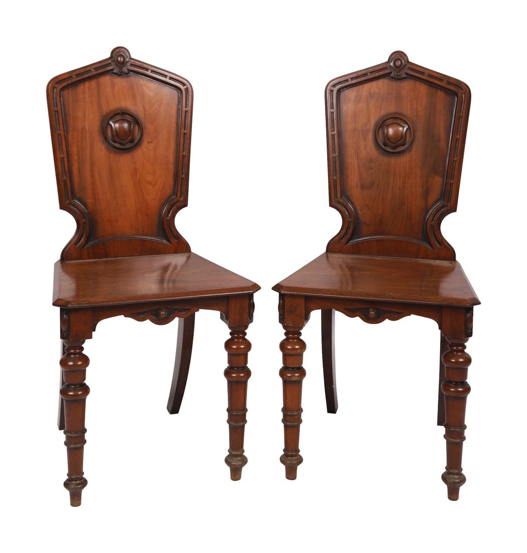 PR 19TH-CENTURY CONTINENTAL MAHOGANY HALL CHAIRS: Each with a shaped back centred with a carved shield motif, above a solid seat and turned supports. FURNITURE