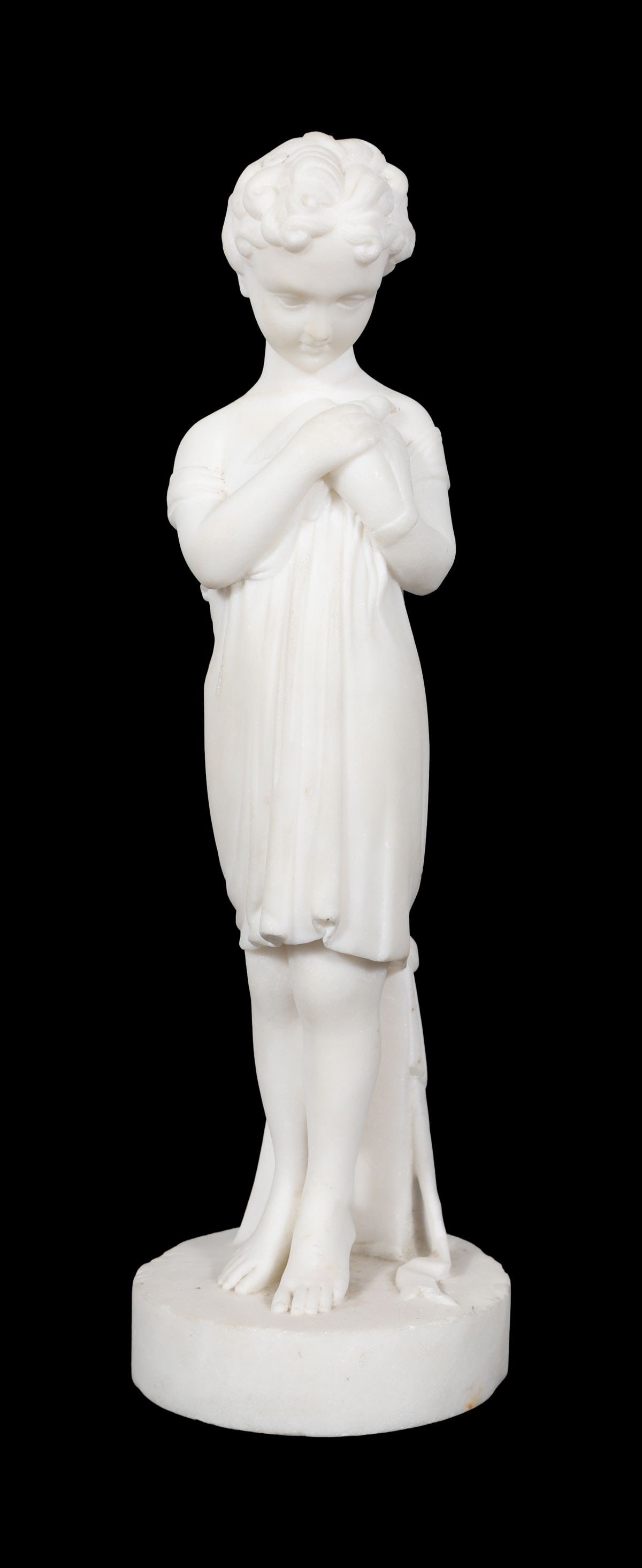 19TH-CENTURY STATUARY FIGURE OF A YOUNG GIRL: A 19th-century white statuary figure modelled as a young girl standing barefoot, her head bowed and hands clasped, draped in a simple classical garment and raised on a circular base. SCULPTURE