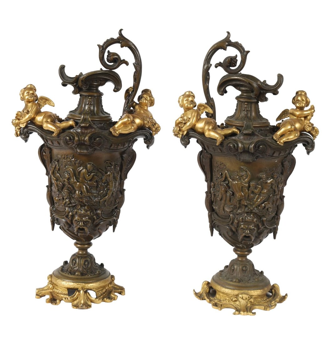 PAIR OF 19TH-CENTURY BRONZE AND ORMOLU URNS: A pair of 19th-century bronze and ormolu urns, each cast with classical relief decoration and applied with scrolling handles, surmounted by putti and raised on circular bases with pierced feet. SCULPT