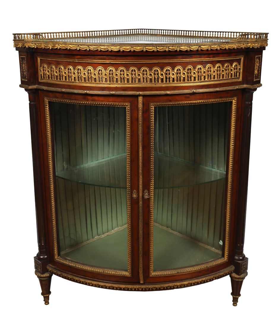 19TH-CENTURY FRENCH ORMOLU MOUNTED CORNER CABINET: the three corner bow fronted marble top above an ornate arched panelled frieze over 2 curved glazed door enclosing a velvet lined interior, between fluted pillars, raised on turned legs. FURNITURE