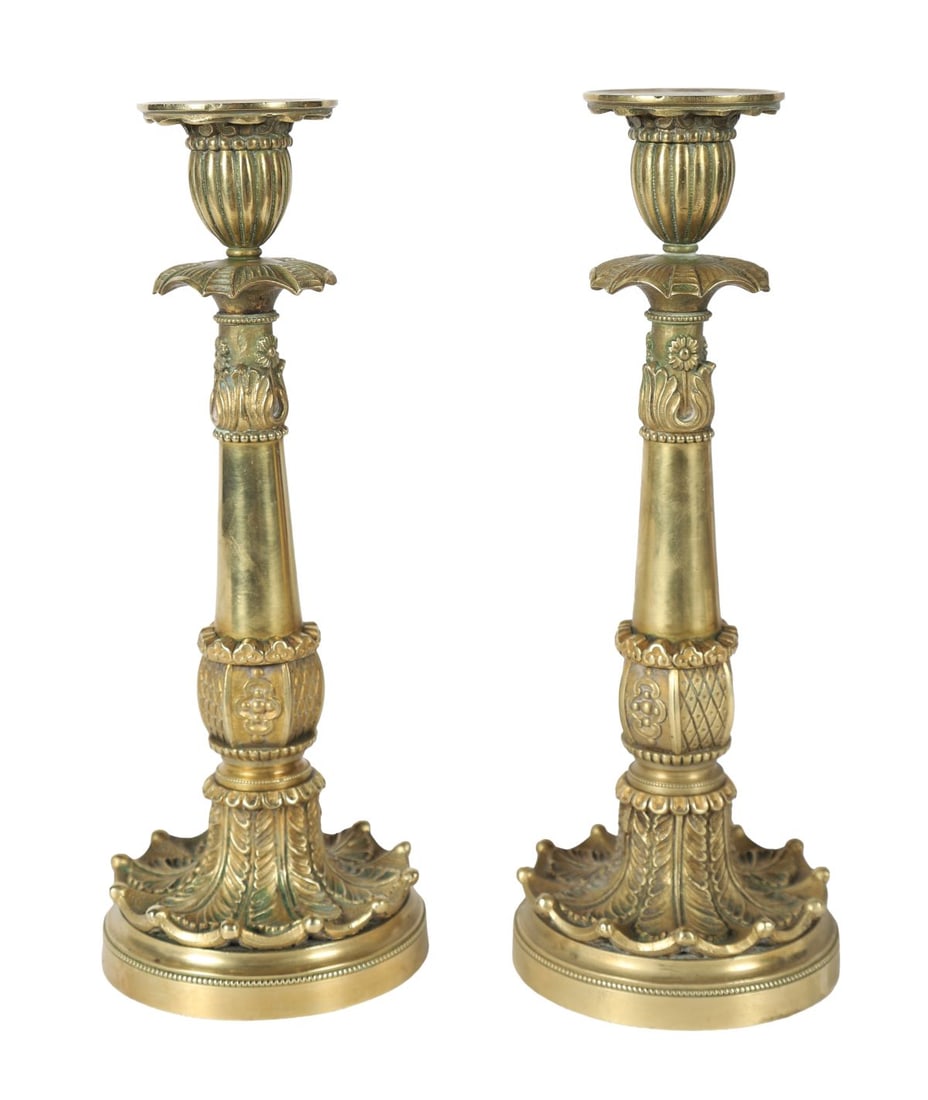 PAIR OF FRENCH EMPIRE PERIOD ORMOLU CANDLESTICKS: A pair of French Empire period ormolu candlesticks, each with circular drip pans above fluted and tapering stems, cast with classical ornament and raised on stepped circular bases with anthemion and b